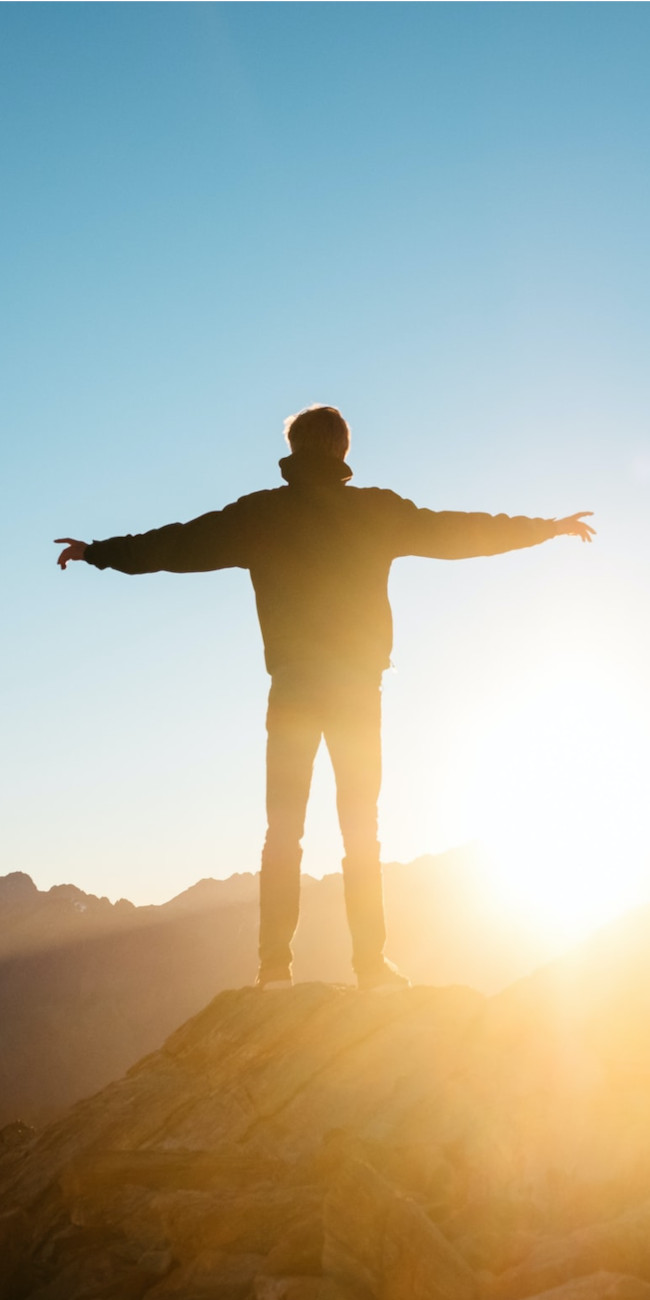 Man standing on mountain celebrating as the sun rises